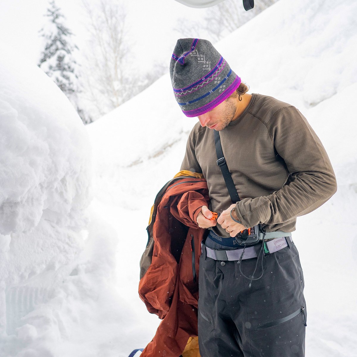 Person in a white/light-colored Capilene baselayer top moving through a snowy alpine landscape.