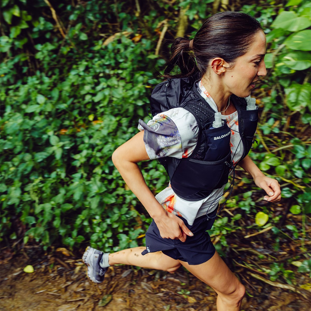 Side view of woman trail running on rainforest trail.