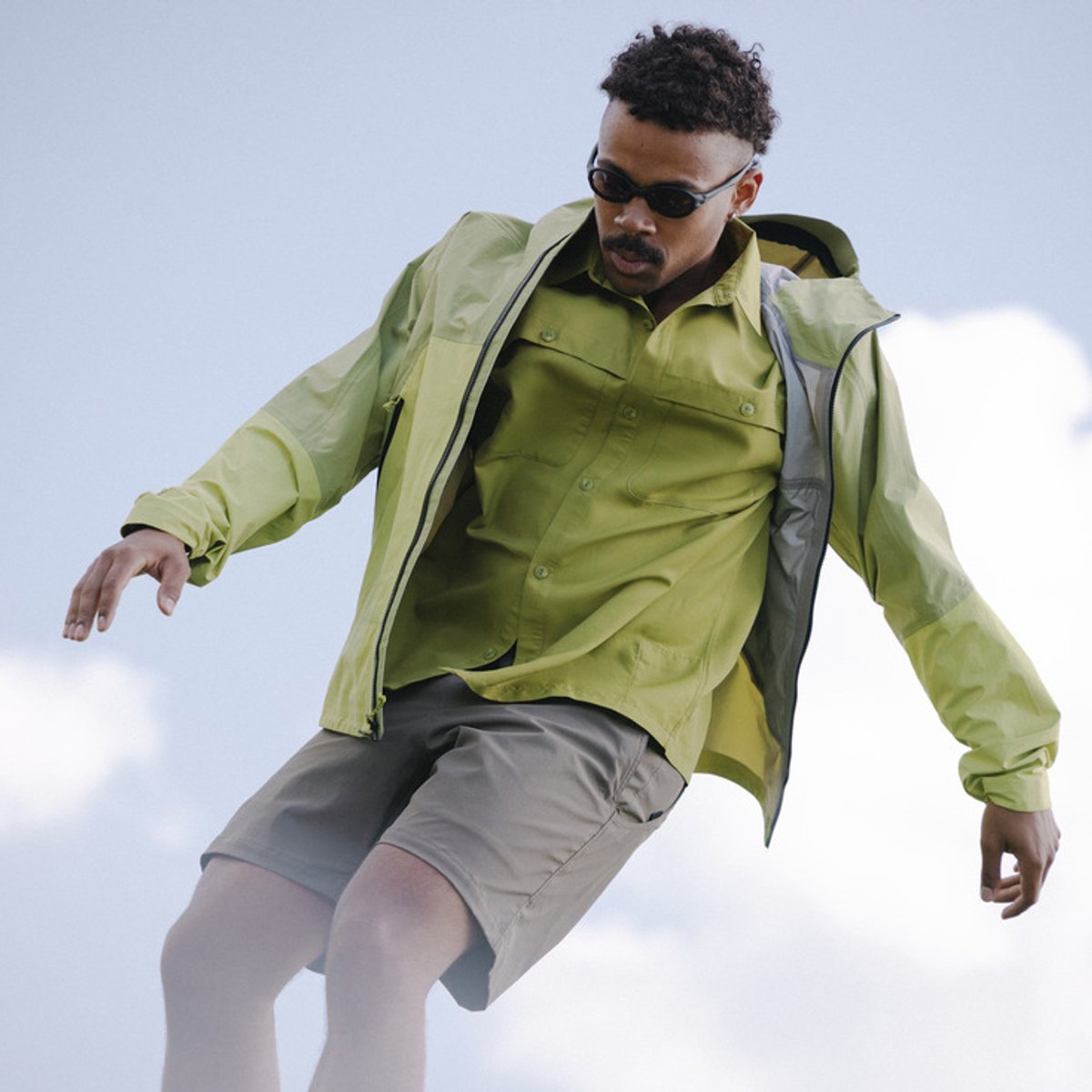 A man stands against a blue sky with clouds, wearing a Mountain Hardwear Sun Drift top.