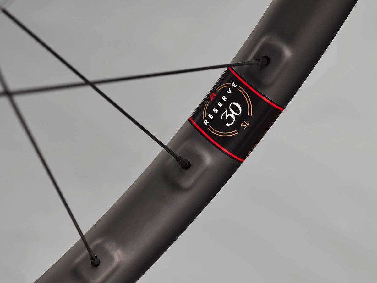Close-up of a Reserve 30 SL carbon mountain bike rim showing the black label with red accent stripe and gold "30 SL" branding, with crossed spokes visible behind.