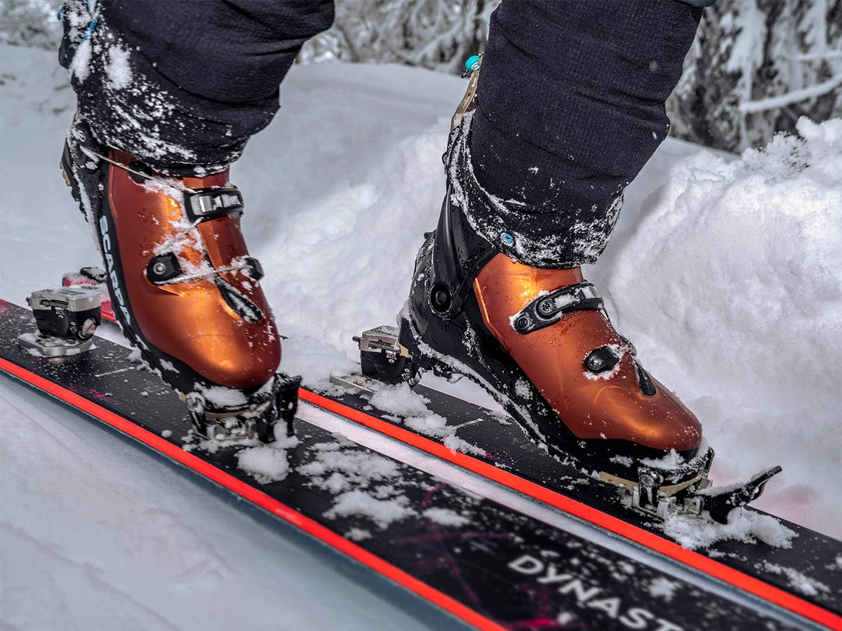 Two SCARPA F1 RS boots clipped into AT bindings on skis, copper-colored shell and cuff construction visible in fresh snow