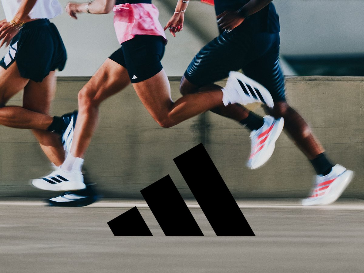 Group of runners racing on paved surface with large Adidas logo between their legs.