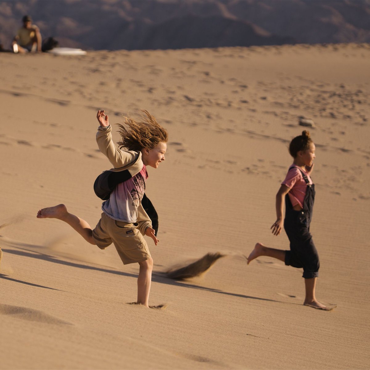 Children playing and running on a sandy beach with clear sunny weather, showcasing outdoor recreational activities and active family fun.