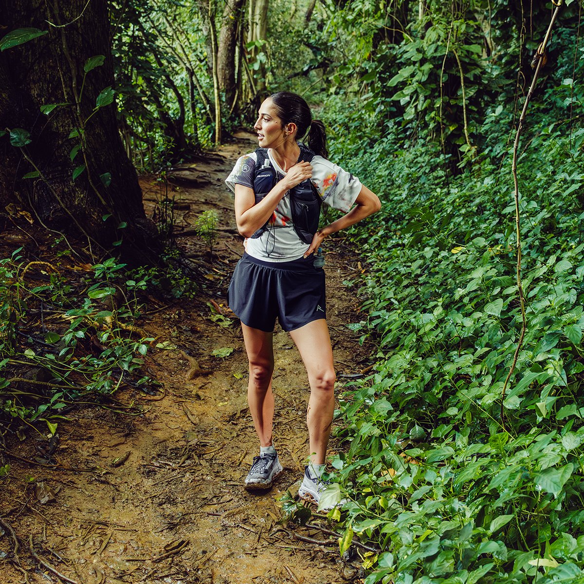 Woman standing on a jungle trail wearing running vest and shoes.