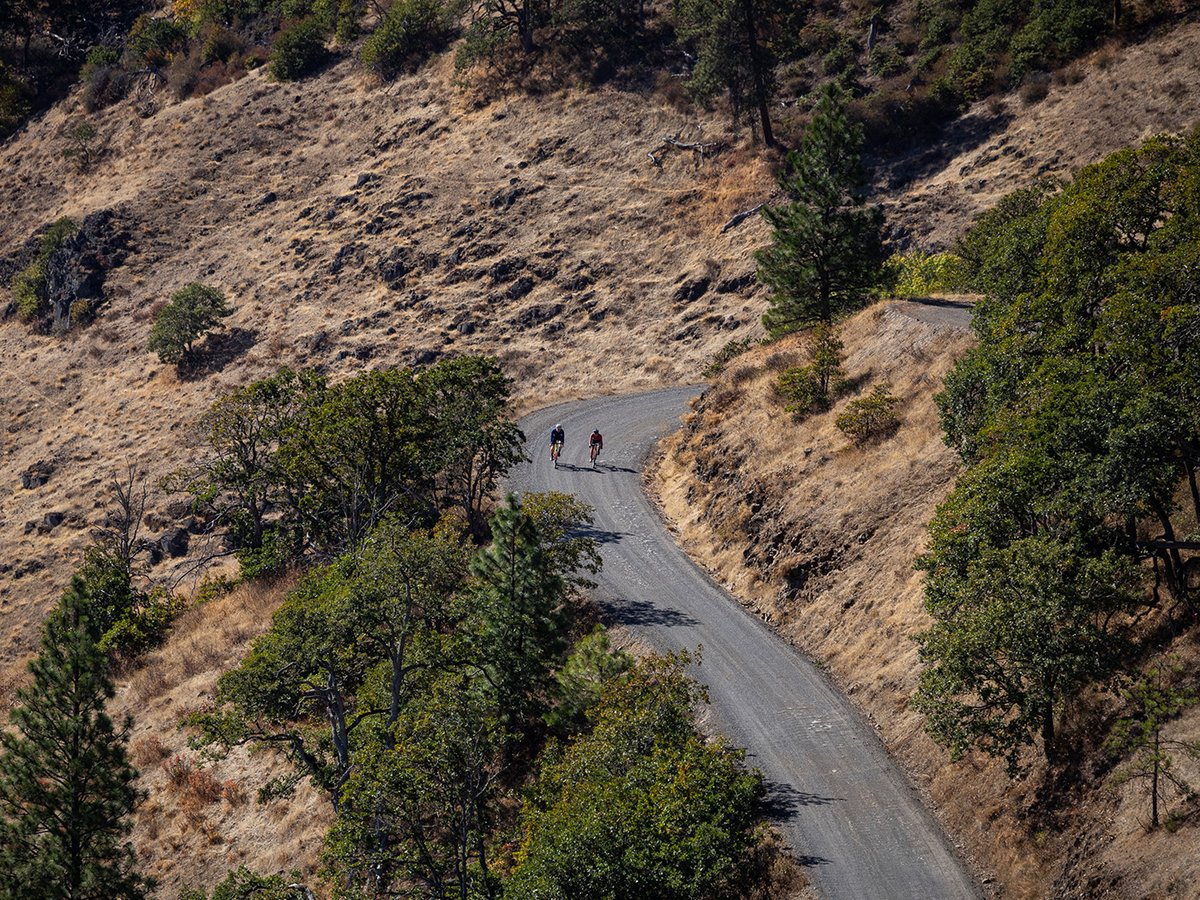 Two cyclicts riding uphill on a curved paved road.