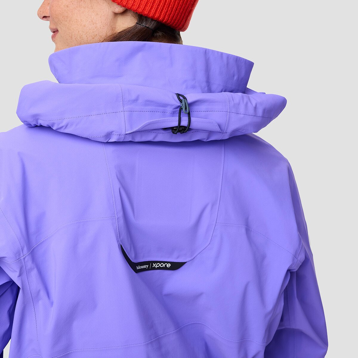 Person wearing ski jacket with hood rolled up and secured to the back of the neck collar.