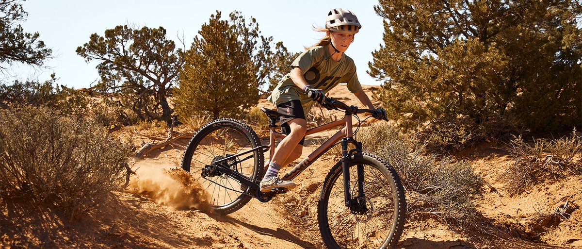 Kid riding Woom Off Air mountaibike fast down a flowy dirt singletrack trail.