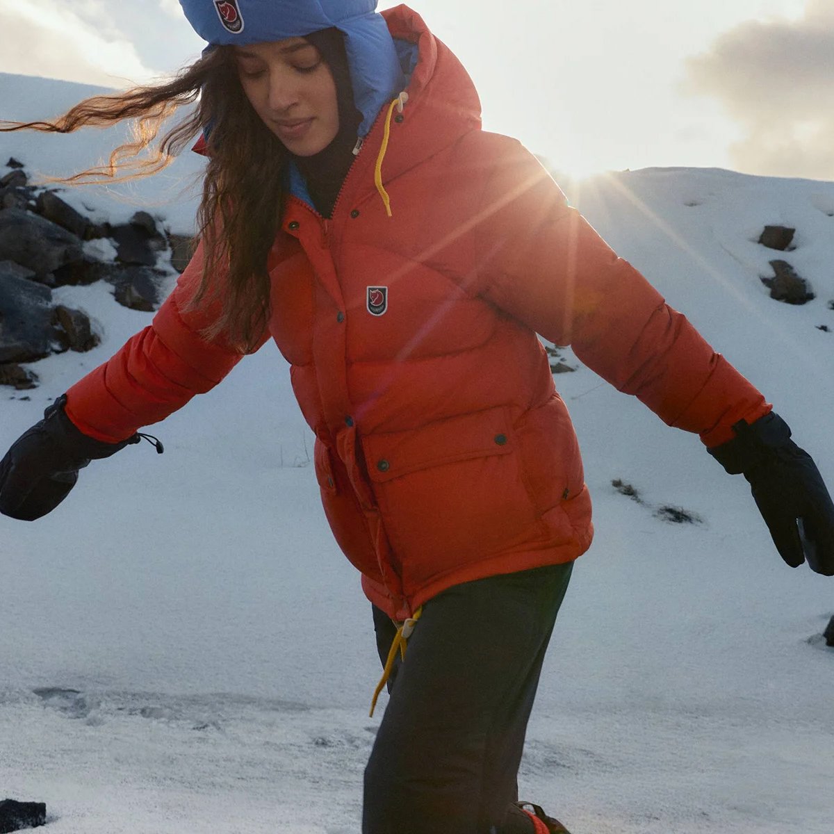 A woman wears a Fjallraven Expedition hoodie against a snowy mountainous background.