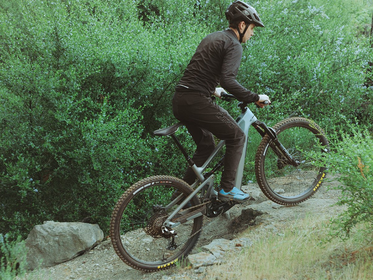 Rider in MTB apparel pedaling full-suspension electric mountain bike on rocky natural trail