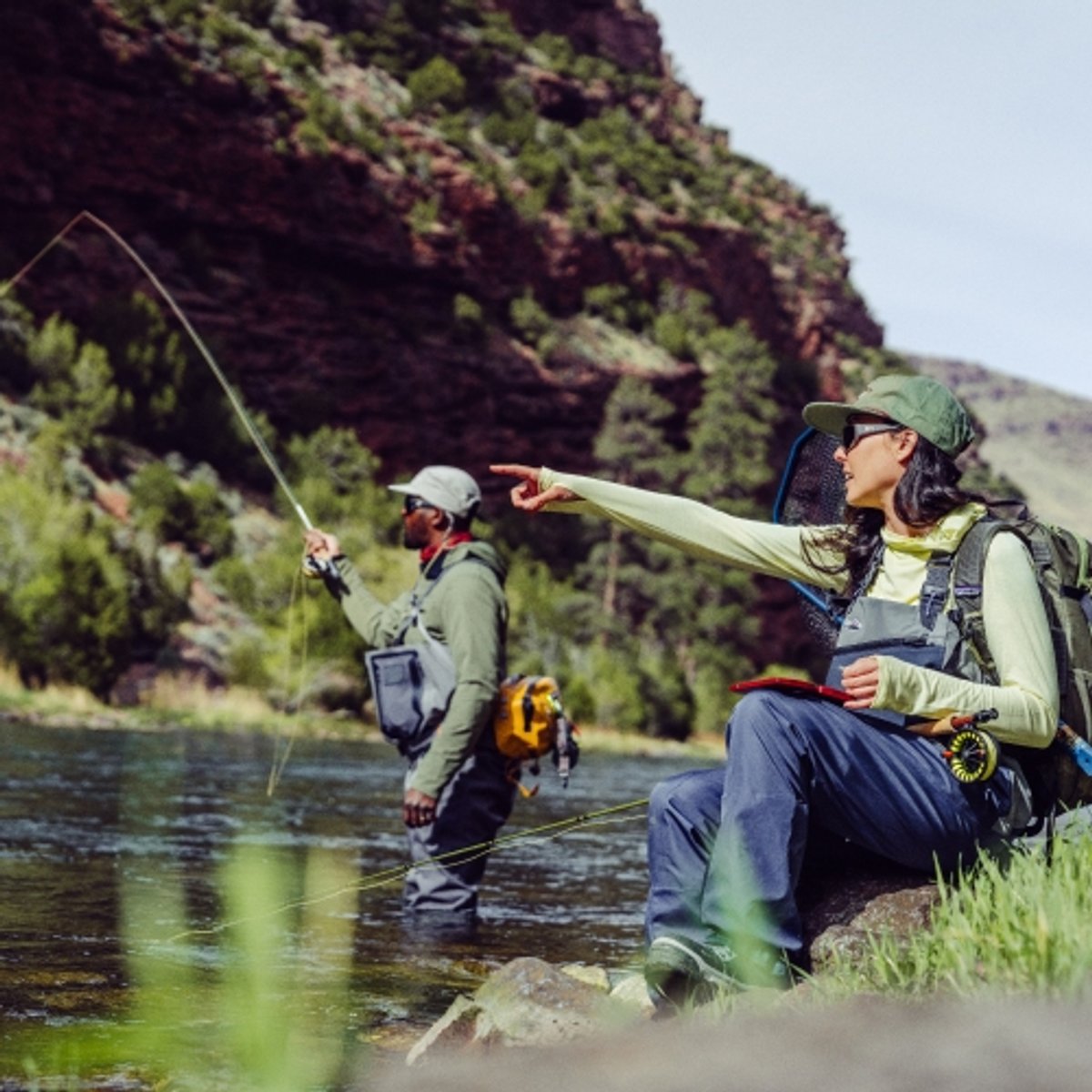 One fly fisher points at the river while the other makes a cast. 