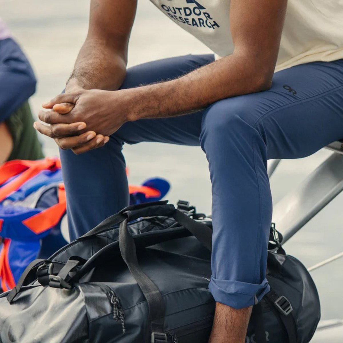 A man wearing Ferrosi Transit Pants sits on a chair, a duffle bag in between his feet.