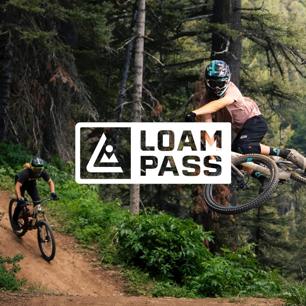 Two mountain bikers on a forested dirt trail — one catching air off a lip, one carving below. Featuring the Loam Pass logo overlaid.