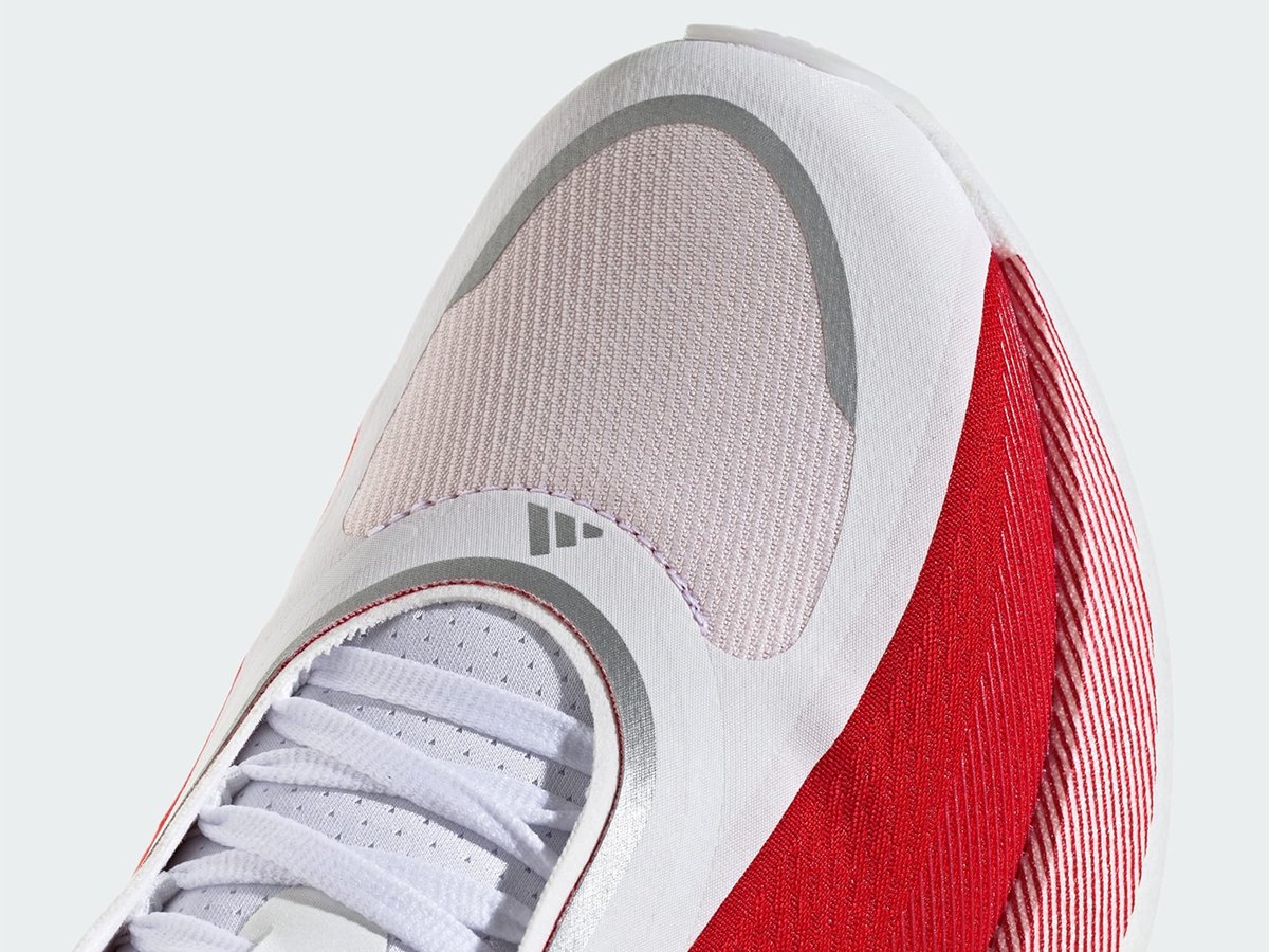 Close-up of an Adidas running shoe toe box showing white knit upper, light pink mesh overlay, gray Adidas logo, and red knit heel panel.