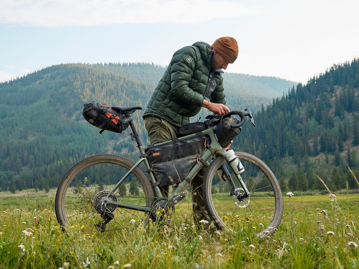 A man leans over his bike in a grassy field.