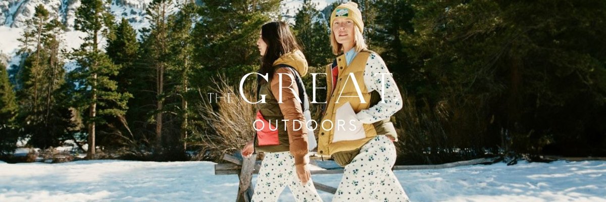 Two women wearing floral print long underwear and colorblocked puffy vests walk in a snowy field.
