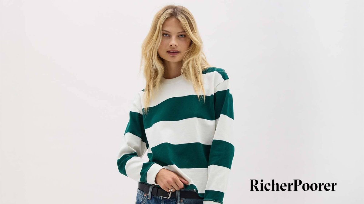 Woman wearing a green and white striped Richer Poorer long-sleeve crew neck sweatshirt paired with dark denim jeans against a white background.