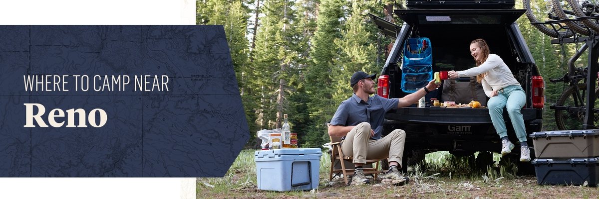 A banner features the text "WHERE TO CAMP NEAR Reno" on a dark blue panel to the left. On the right, a man and a woman share food while seated at the open tailgate of a black pickup truck, which is set up for camping in a forest clearing with camping supplies, storage boxes, and a cooler nearby. Tall green pine trees fill the background.