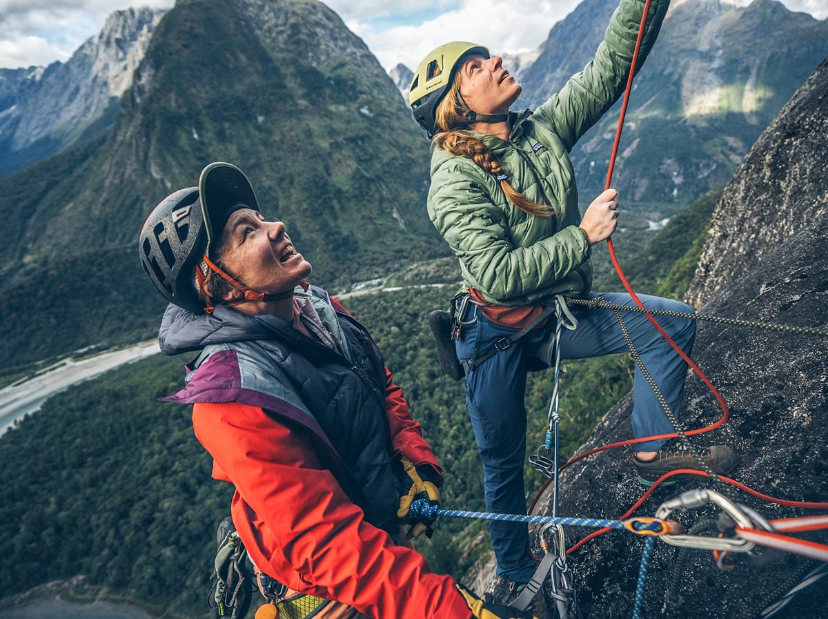 Two rock climbers scale a mountain with the white "patagonia" logo written over the center of the image.