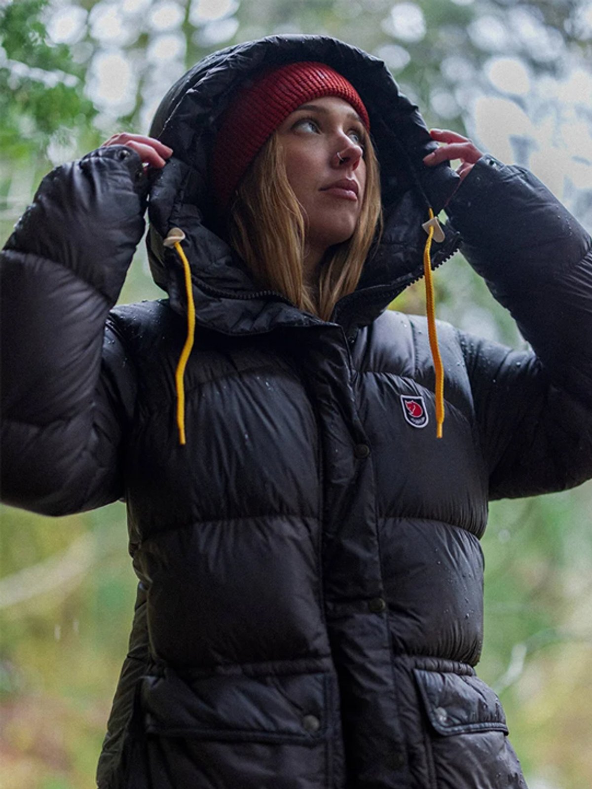 A woman wears the Fjallraven Expedition Long Down Parka with the hood up.