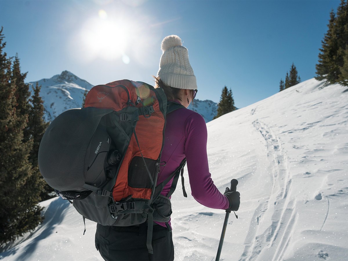 Skier skinning uphilll with poles and fully packed backpack.