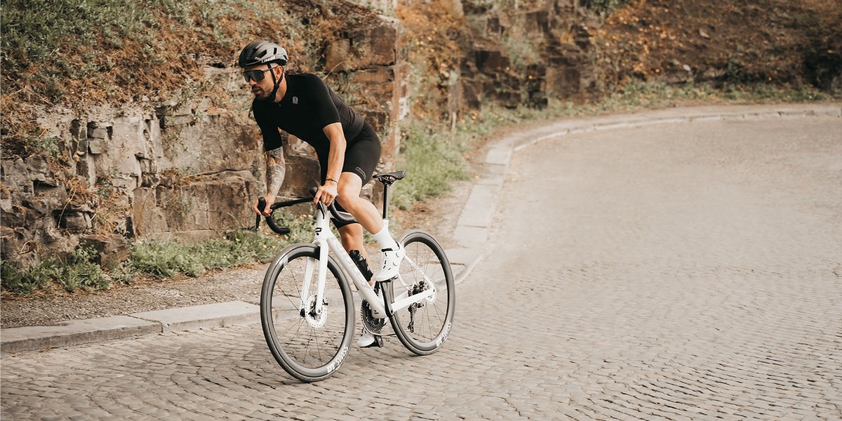 Cyclist riding Ridley Falcn down curved cobblesstone road.
