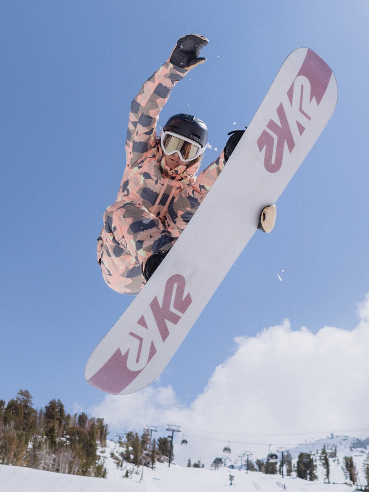 A snowboarder does a grab mid-air, showing off the base of her K2 board.