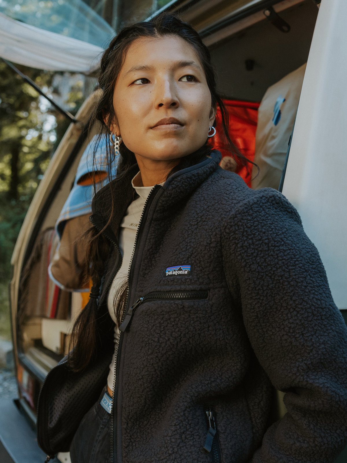 A woman wearing a dark gray Patagonia fleece jacket over a light shirt hangs out at camp.