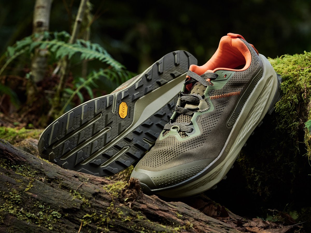 The New Altra Olympus 7 trail running shoe displayed on a mossy log in a forest setting.