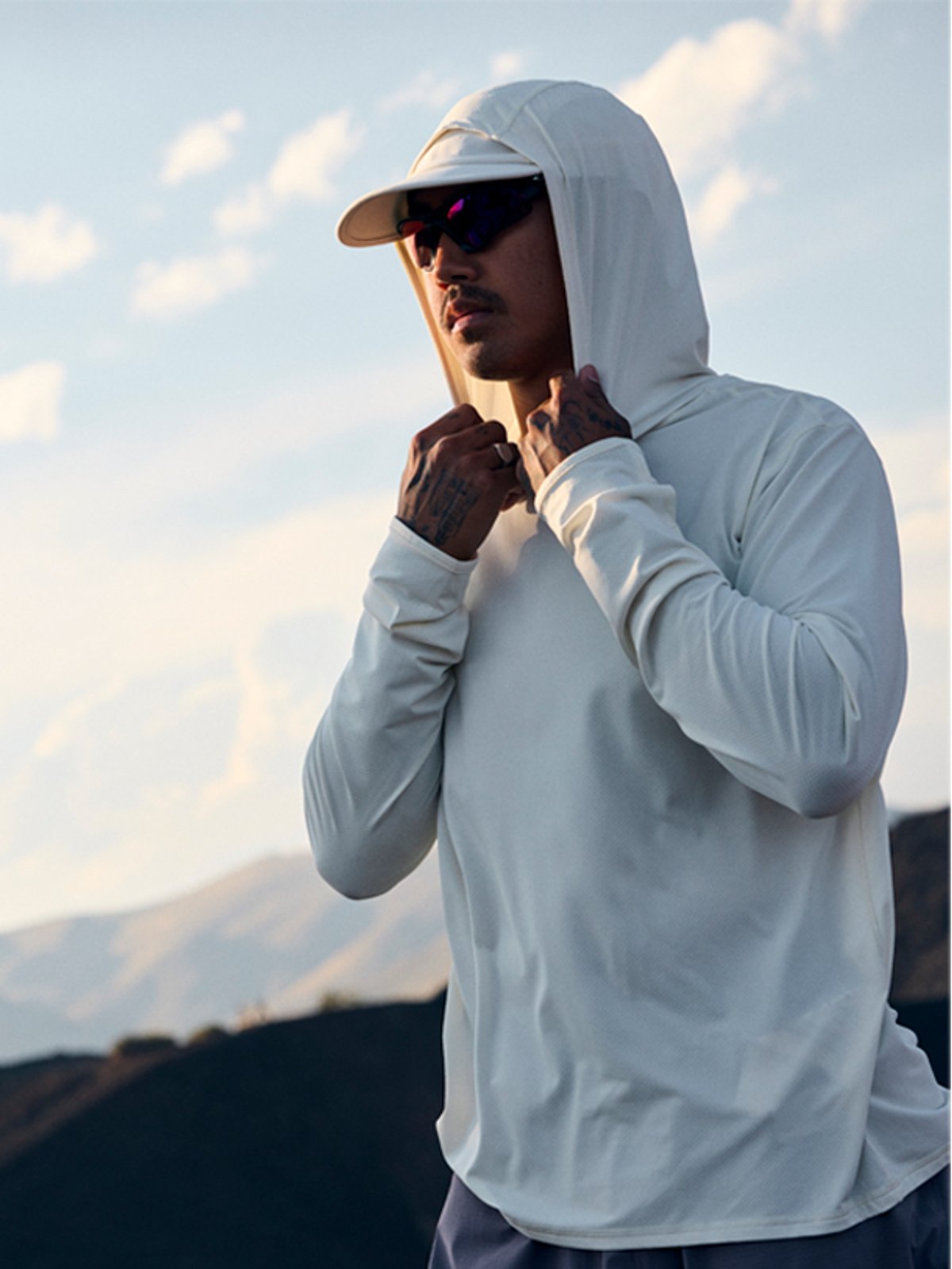 A man wearing a Tahoe Sun Hoodie with the hood up stands against a backdrop of clouds
