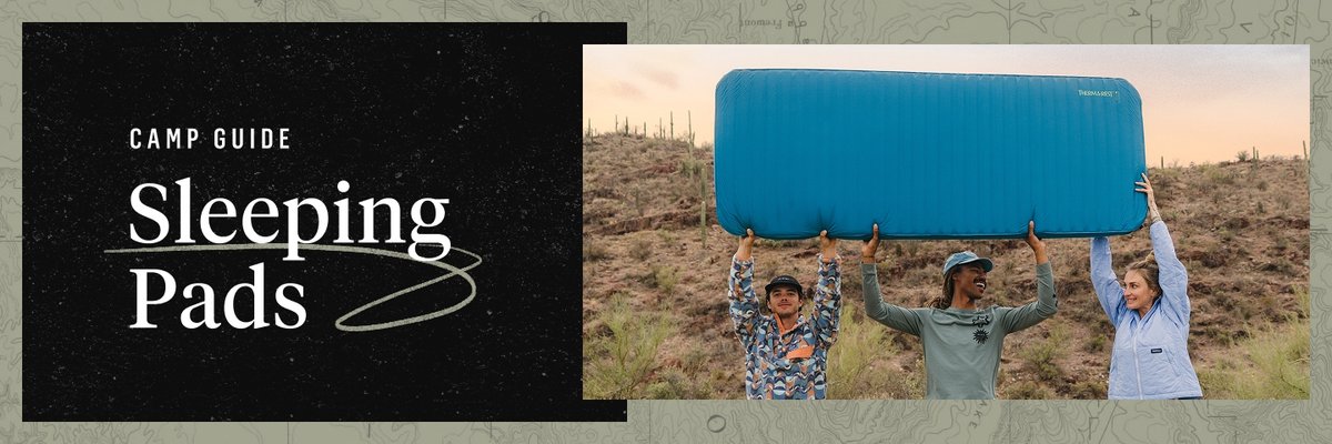 Three people hold up a huge, blue, camp sleeping pad. They’re laughing. Desert hills with cacti rise in behind them. Words appear to the left of the people saying “Camp Guide, Sleeping Pads”.