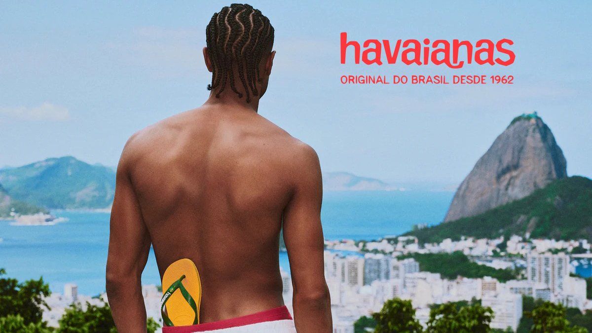 Man wearing yellow Havaianas flip-flops overlooking Rio de Janeiro beach with iconic mountain peak in background.