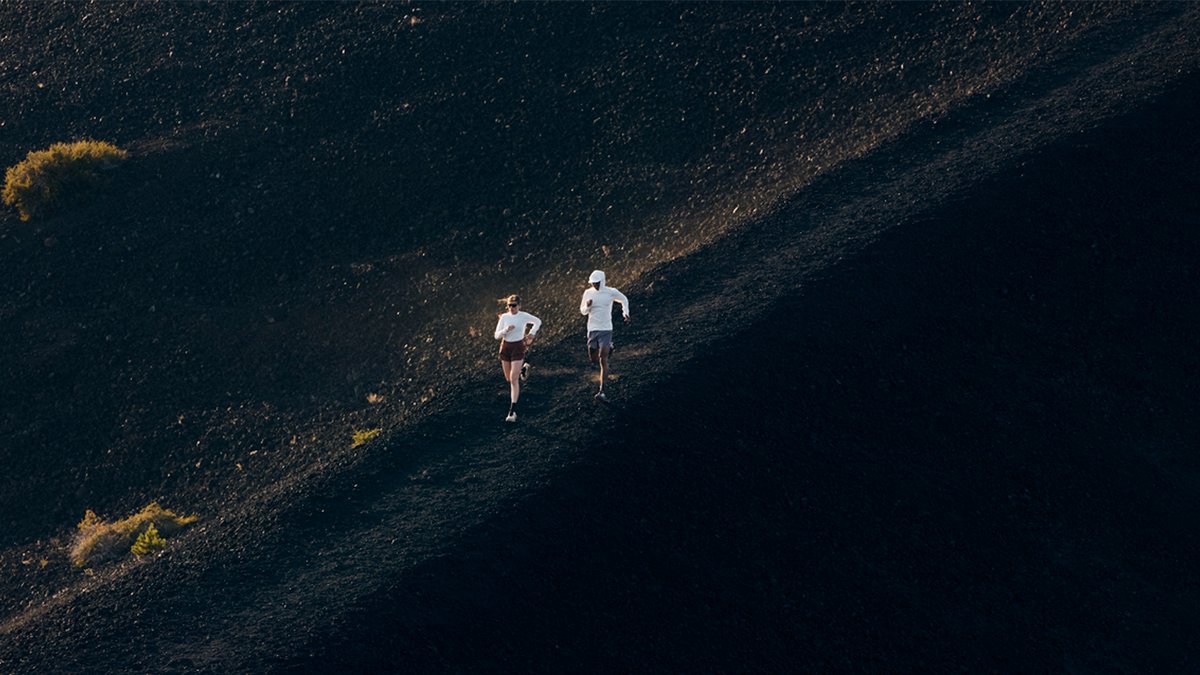A man and a woman wearing the BGA Tahoe Sun line run down a rocky decline.