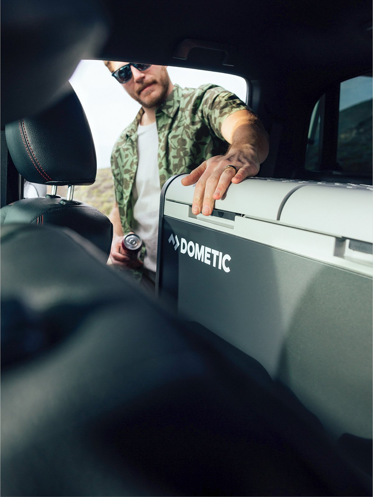 A man is retrieving a beverage from a cool that’s in the back of a vehicle.
