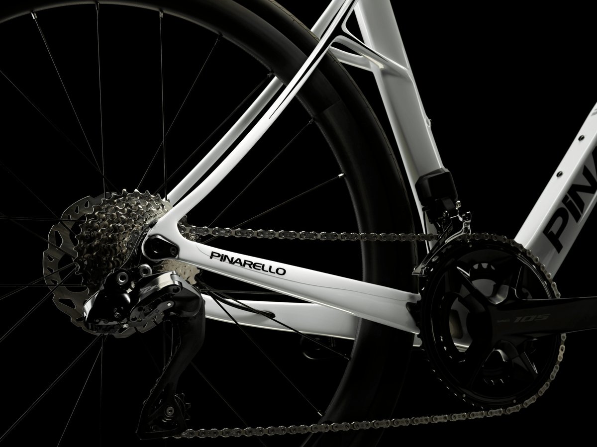 Pinarello white carbon road bike Onda fork and disc brake rotor detail with deep section front wheel against dark studio background