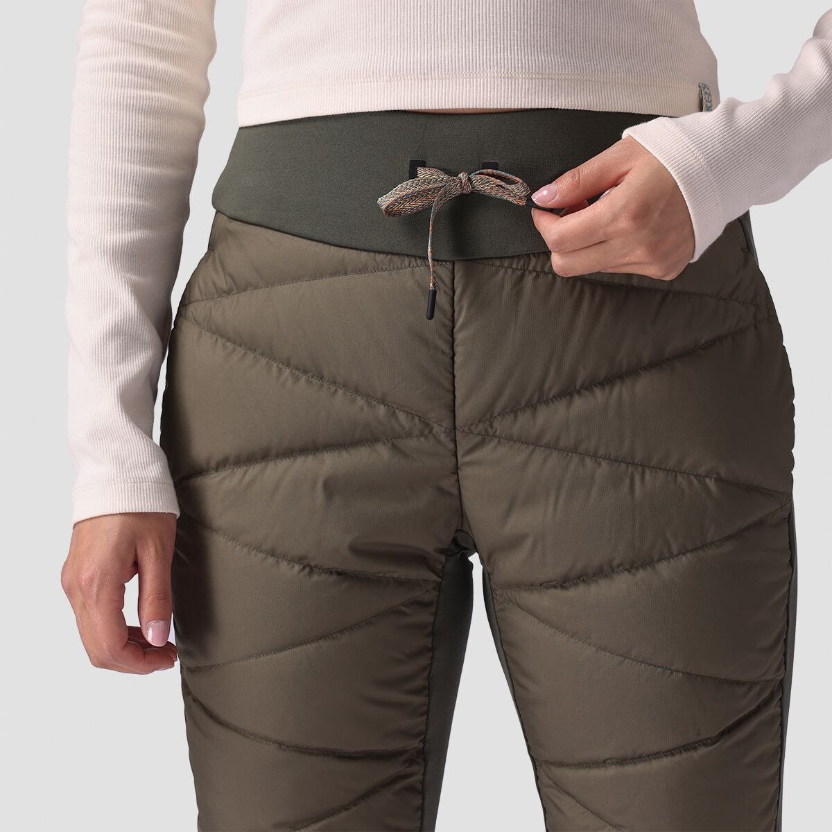Close-up of a woman's waist adjusting the drawcord on Stansbury ALLIED Down pants, showing the diagonal zig-zag baffle quilting pattern.