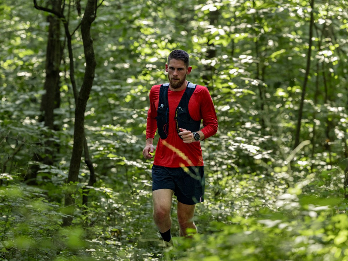 A man wearing a running vest runs through a forest.