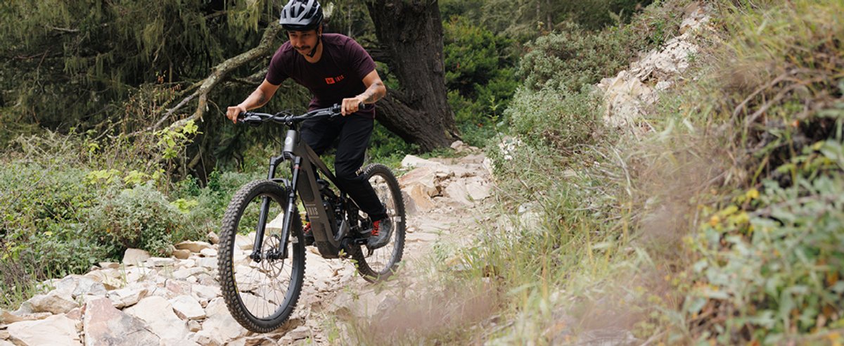 Mountain biker pushing through rocky exposed trail section on electric mountain bike in open scrubby terrain