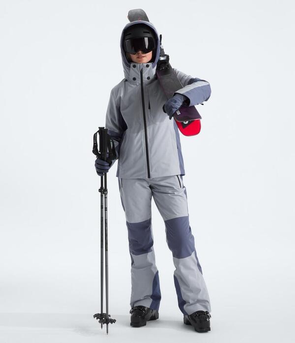 Person wearing helmet and and goggles under snow jacket and pants with ski boot holding skis and poles.