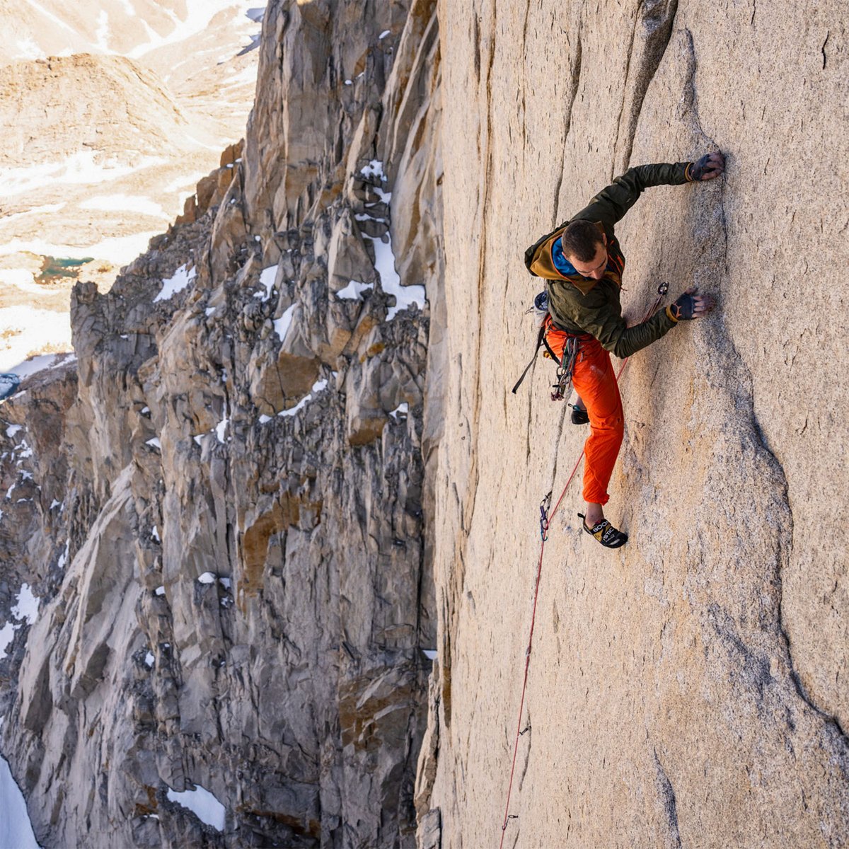 Trad climber wearing abrasion-resistant stretch climbing pants climbing up steep granite wall on exposed alpine big-wall route
