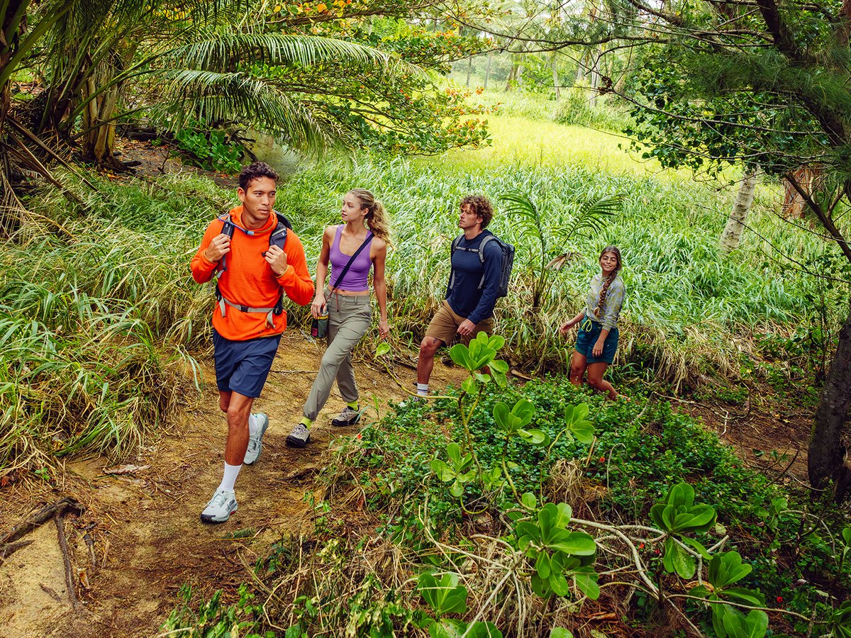 Group of four people hiking on trail in rainforest wearing ripstop bottoms and outdoor gear.