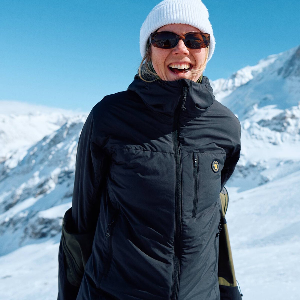 A smiling woman wearing sunglasses shows off her coat.