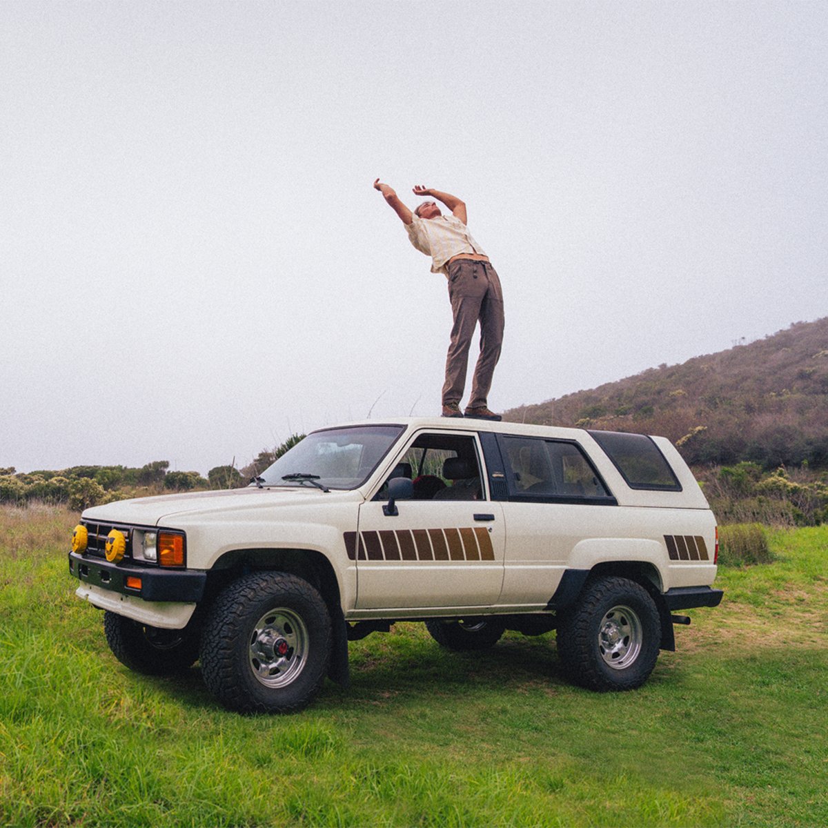 A man stands on top of a sedan, bending backwards while wearing prAna Stretch Zion pants.