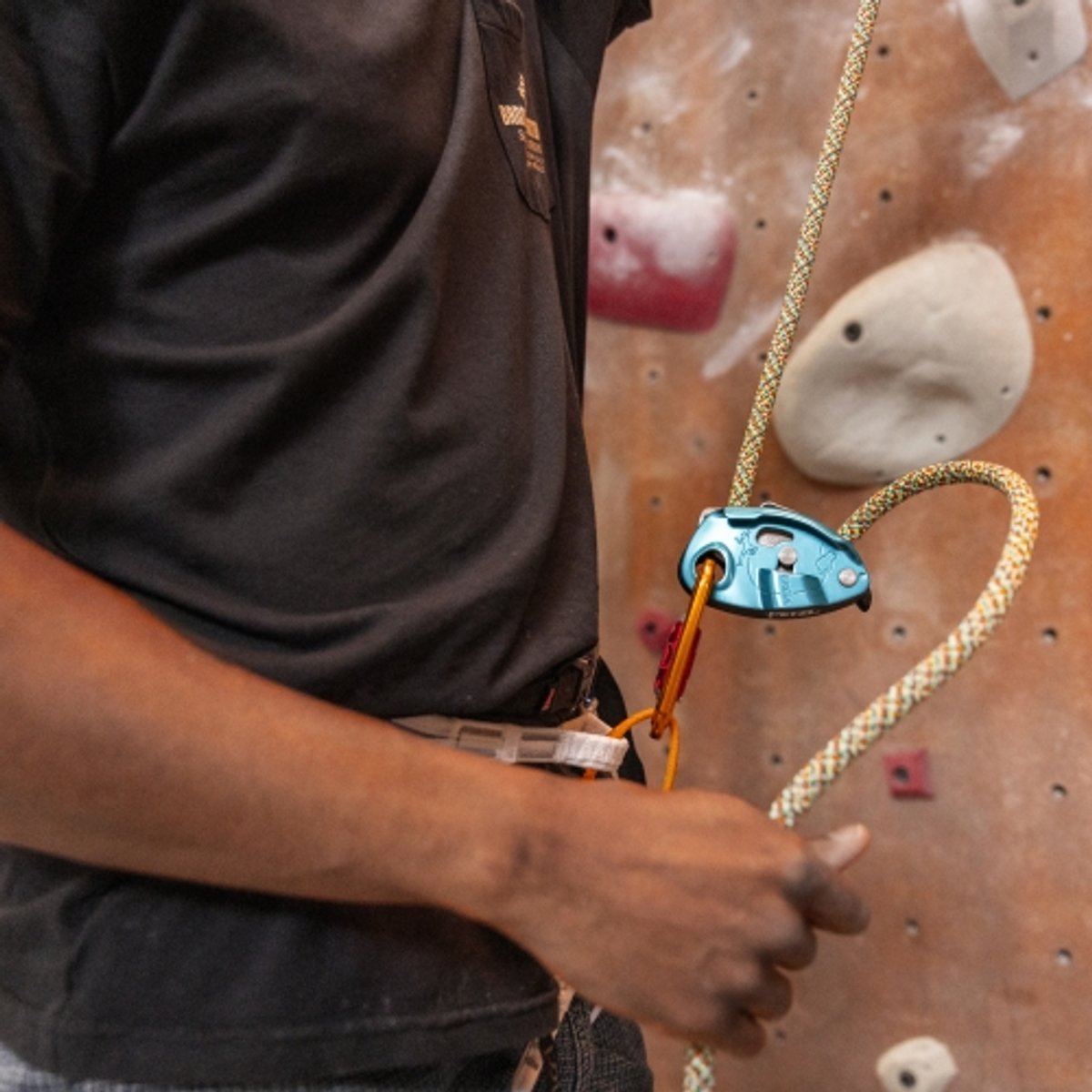 A rock climber operates a belay device at an indoor climbing gym. 