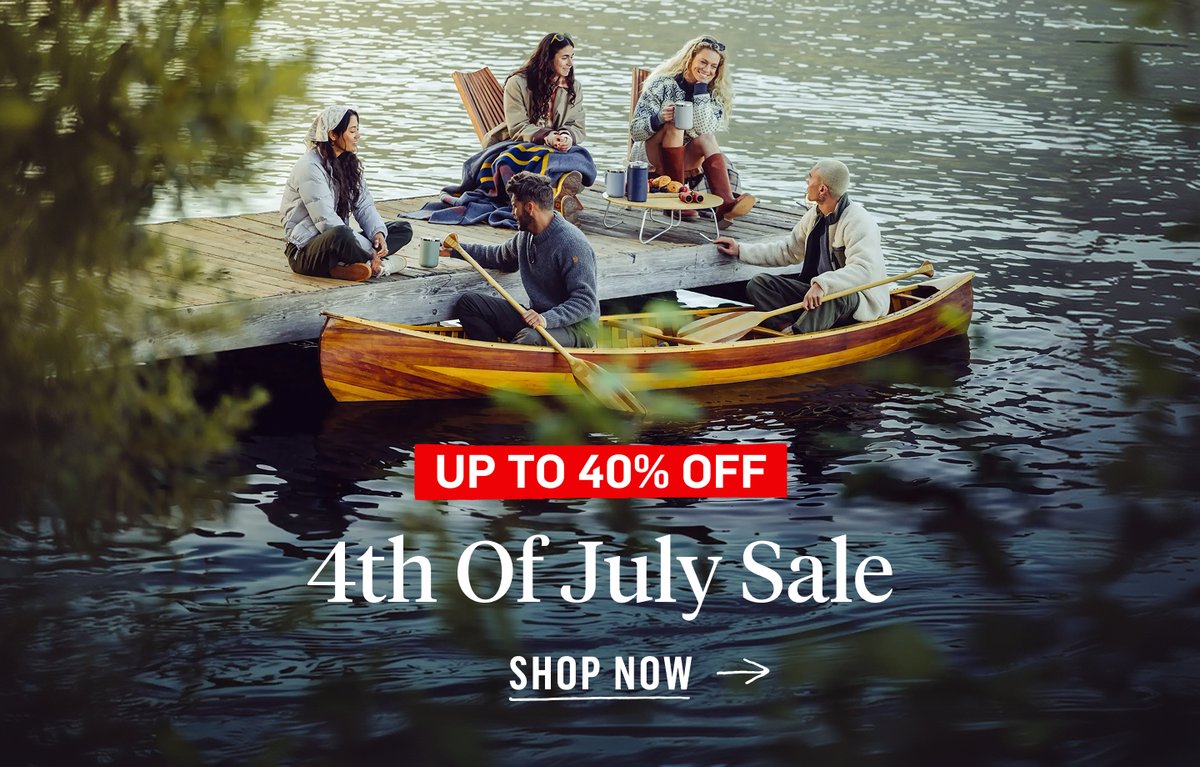 A group of friends relaxing on a lakeside dock and wooden canoe in outdoor apparel. 4th of July Sale — up to 40% off.