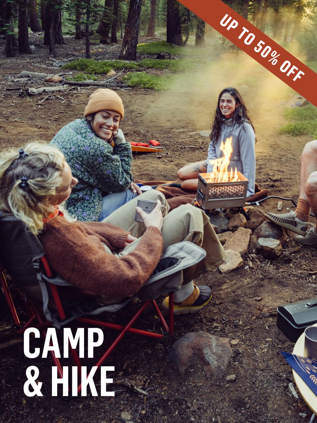 Friends gathered around a portable camp stove in a misty pine forest, laughing and warming up with hot drinks. Up to 50% off Camp & Hike.