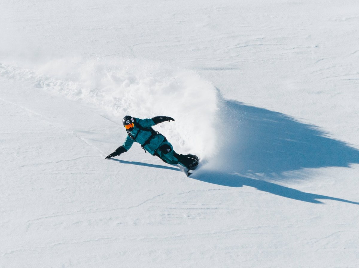 Snowboarder in a teal kit laying a deep carve through fresh powder.