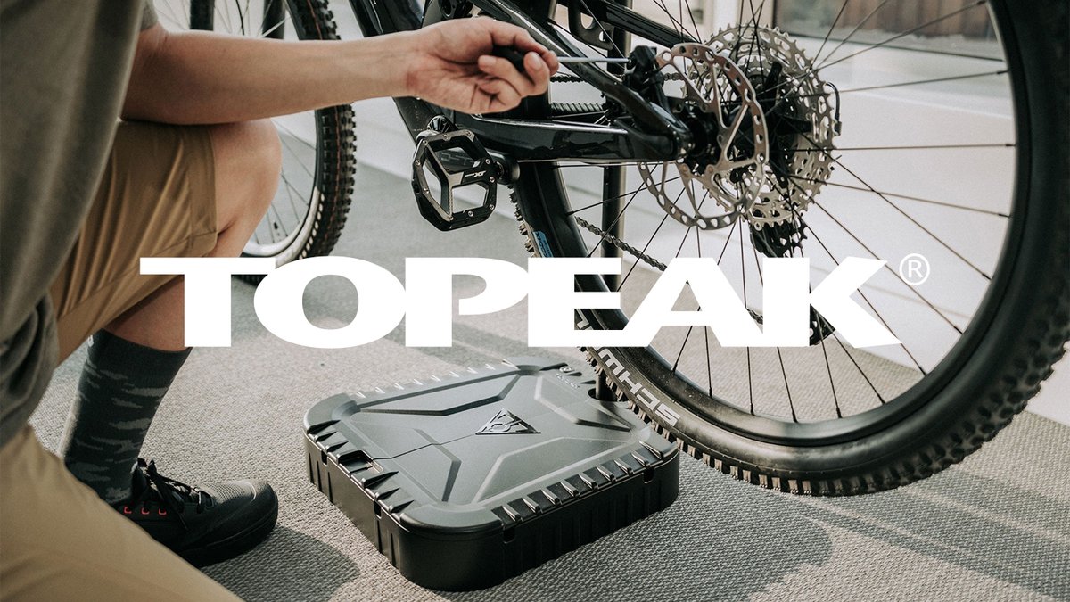 Person performing bicycle maintenance on a mountain bike drivetrain with a Topeak repair toolbox on the ground.
