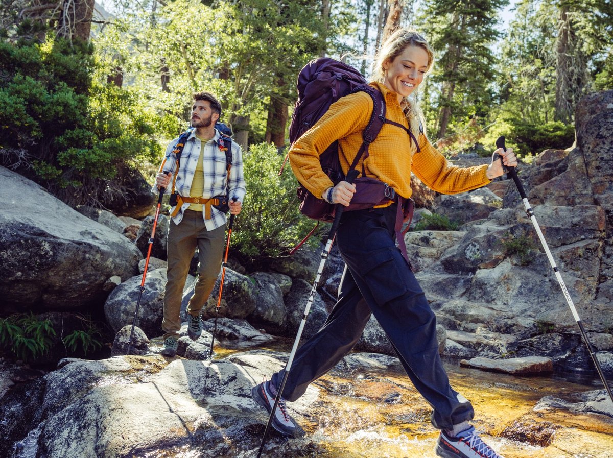 Two hikers on a rocky forest trail with trekking poles and loaded packs.