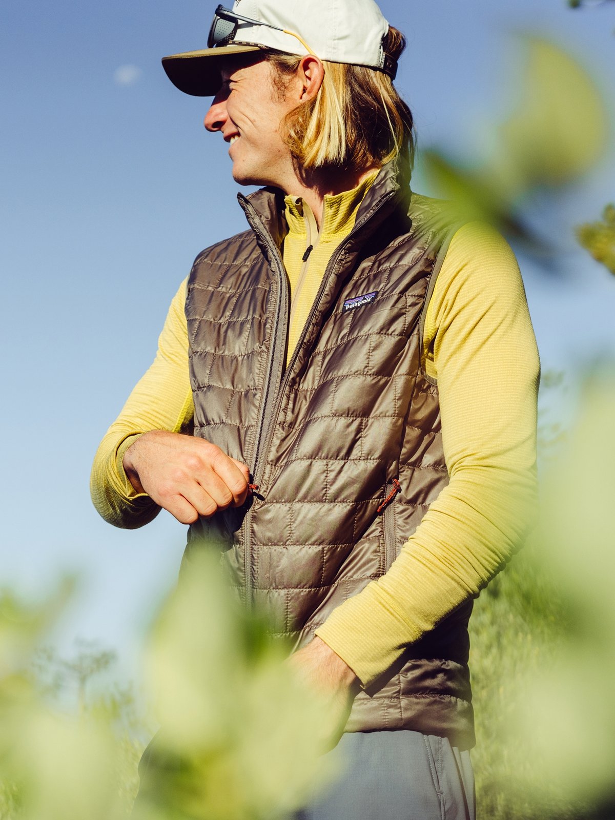 A hiker wearing a yellow long-sleeve shirt, and a brown quilted vest.