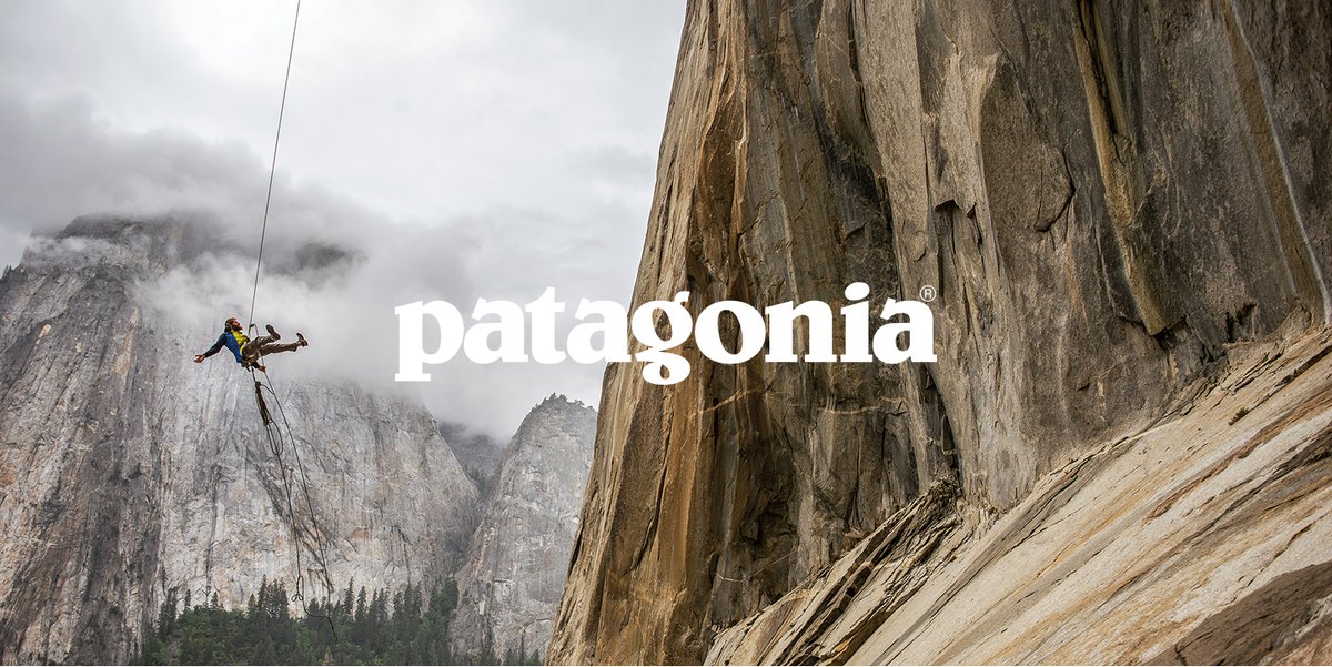 A person swings on a rope near a large cliff face. The word, “patagonia” is over the cliff.